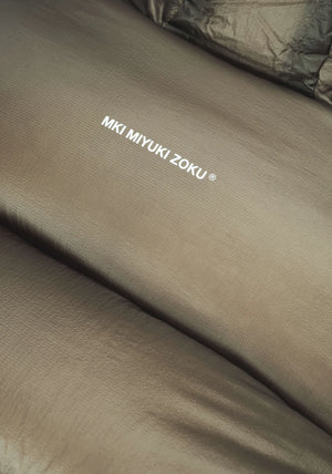 MKI MIYUKI ZOKU Translucent Bubble Jacket In Khaki at EQVVS Menswear. Logo Detail Shot. 