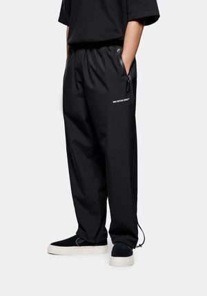 Loose Fit V2 Shell Track Pants in Black by MKI MIYUKI ZOKU at EQVVS. Side Model Shot.